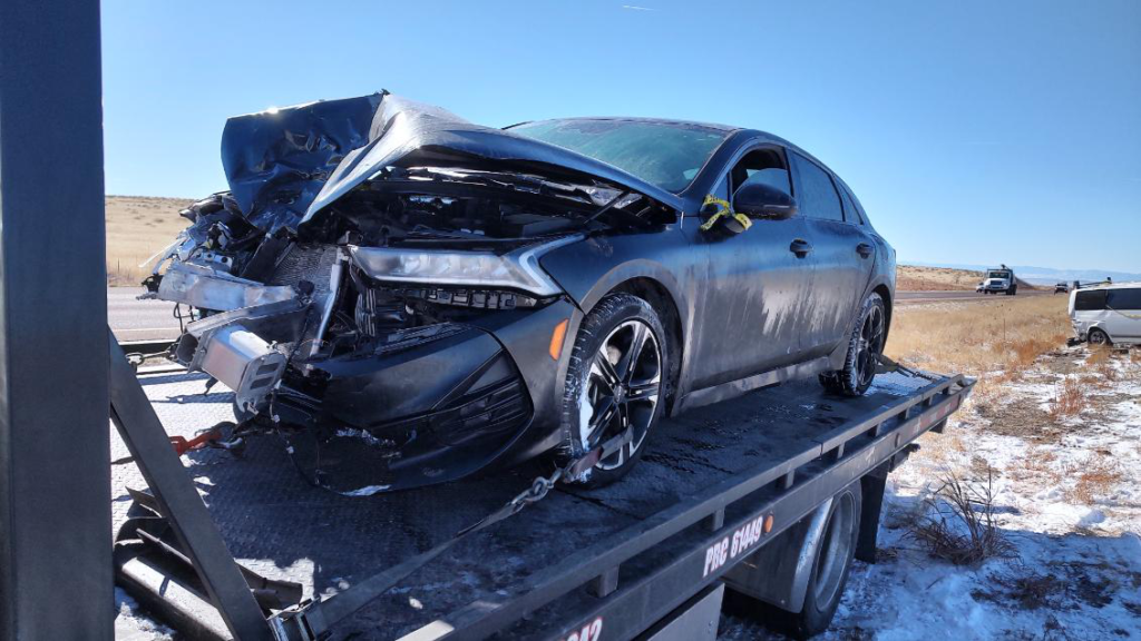 A wrecked car on a tow truck in a snowy area, highlighting the importance of family road trip safety in winter conditions.
