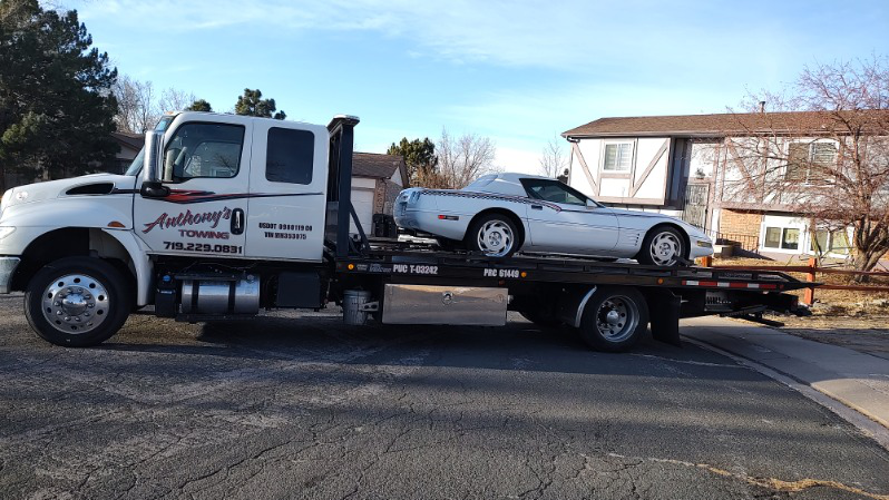Silver convertible car loaded on a tow truck in a residential area.