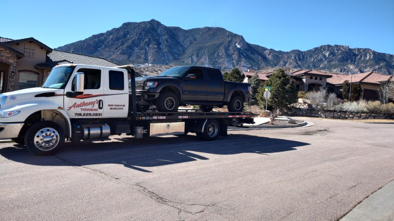 Dark grey pickup on a tow truck against mountains, ensuring family road trip safety.