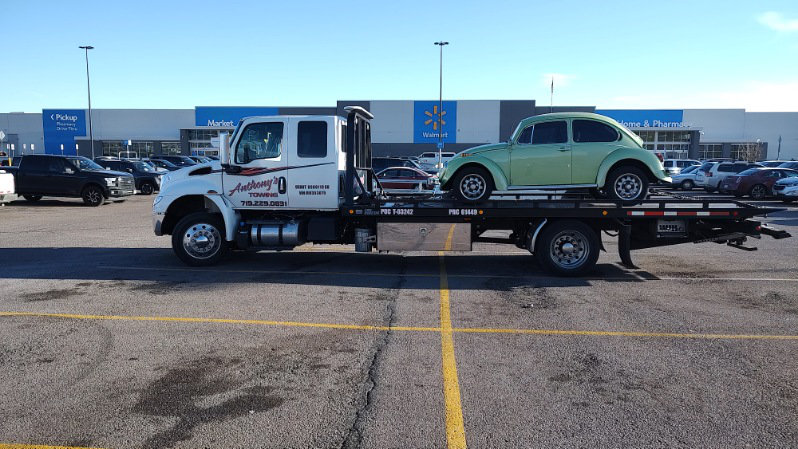 Light mint green VW Beetle on a tow truck in a Walmart parking lot. Family road trip safety is essential even during pitstops.