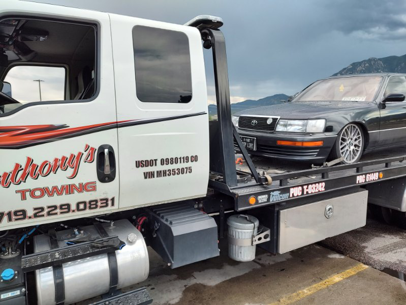 Amidst stormy skies and mountain views, a black car gets expert assistance on a tow truck, ensuring a safe and reliable journey during a holiday road trip plan with Anthony's Towing.