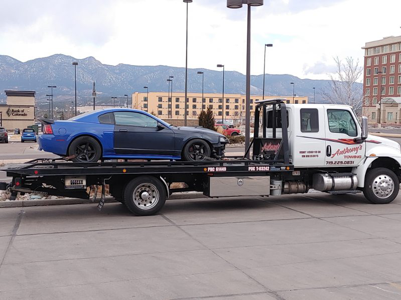 A striking sports car being towed in a lot with urban elements, street lights, and picturesque mountains in the background.
