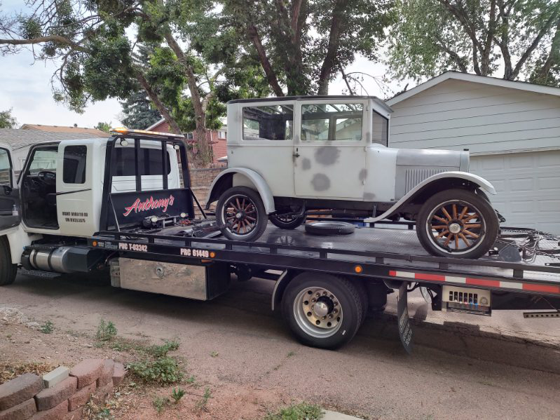 A vintage car and tire loaded onto Anthony's Towing tow truck in a residential area trusts reliable towing during the holidays.