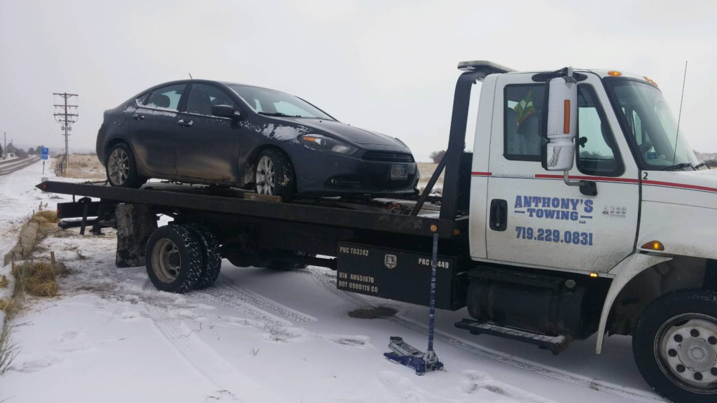 A black sedan securely loaded onto an Anthony's Towing tow truck against a backdrop of pristine snow.