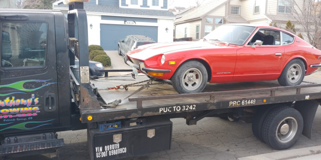A vintage red car securely loaded on an Anthony's Towing tow truck in a residential area, emphasizing the reliability of their affordable towing service.