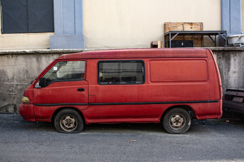 A red van parked on the street with a flat front tire