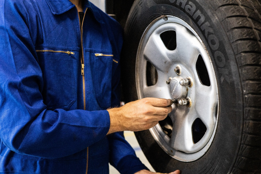 A person in a blue jacket supports a tire while removing bolts