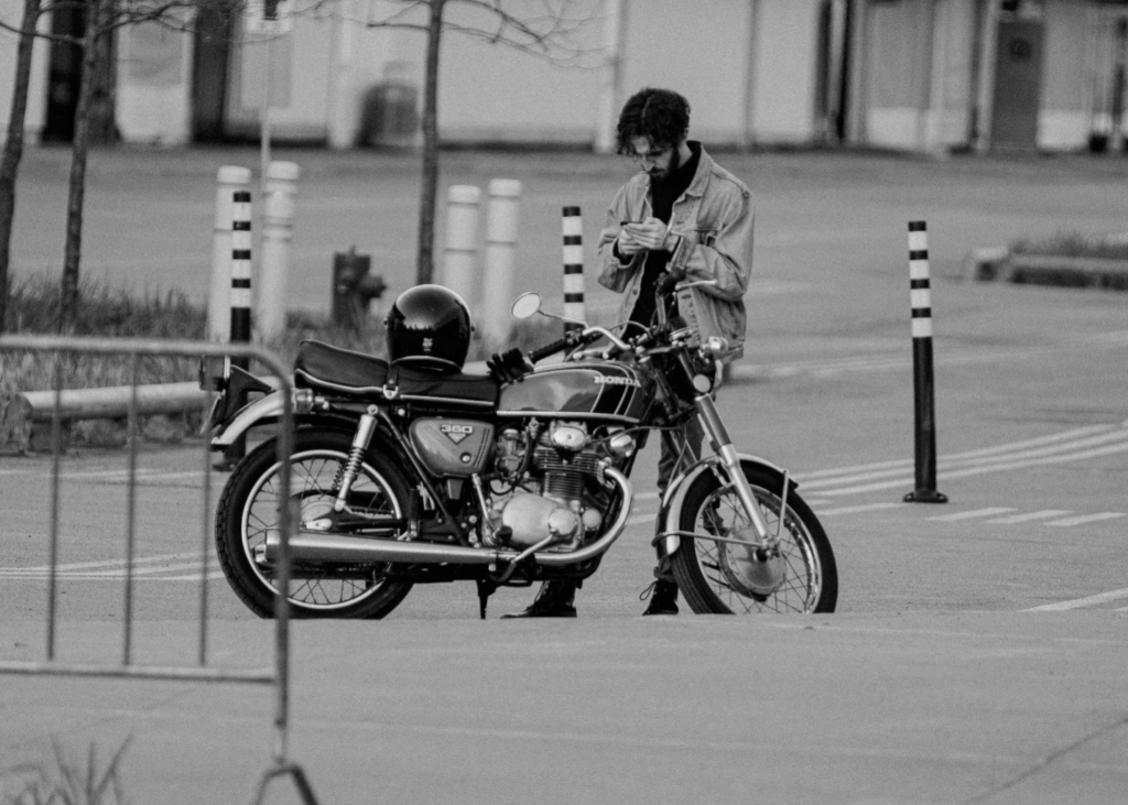 Rider uses his phone next to his motorcycle by the curb in a black and white photo