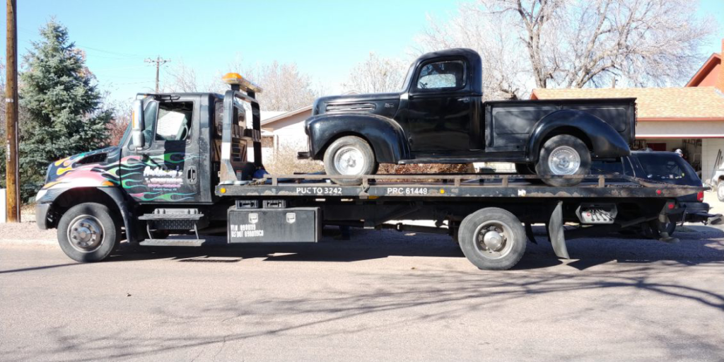 A reliable Anthony's Towing tow truck brings a black pick up truck to a workshop