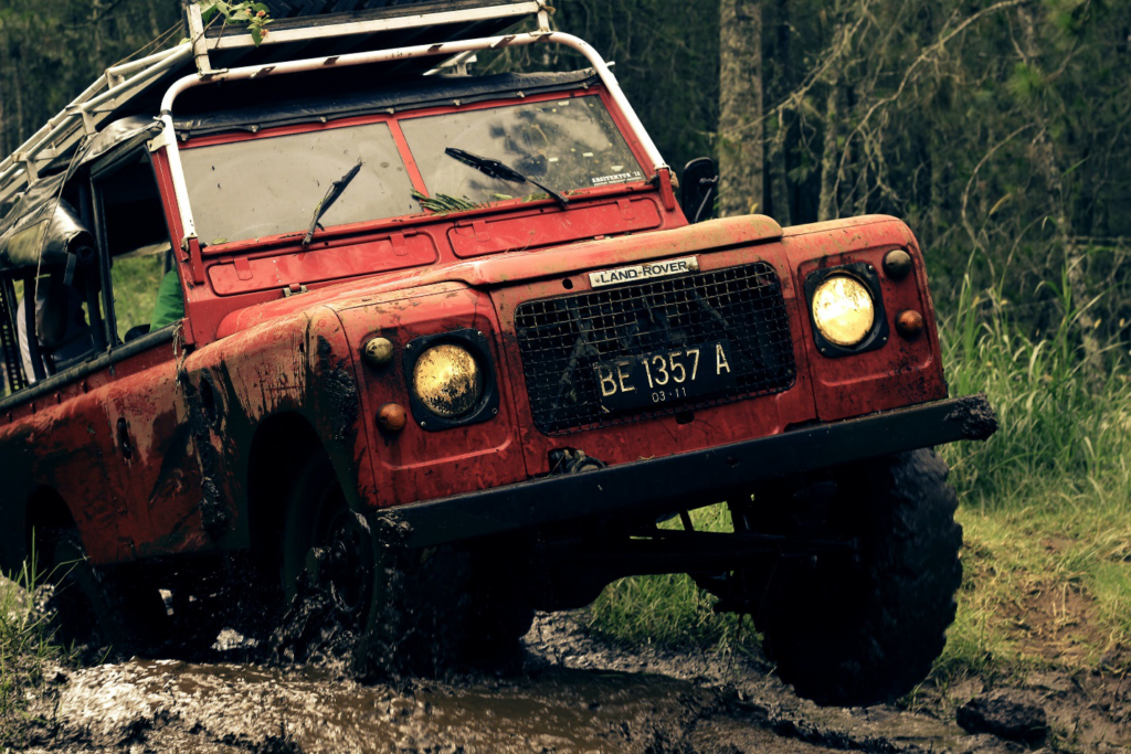 A red Land Rover stuck on a muddy road near trees and marshy land