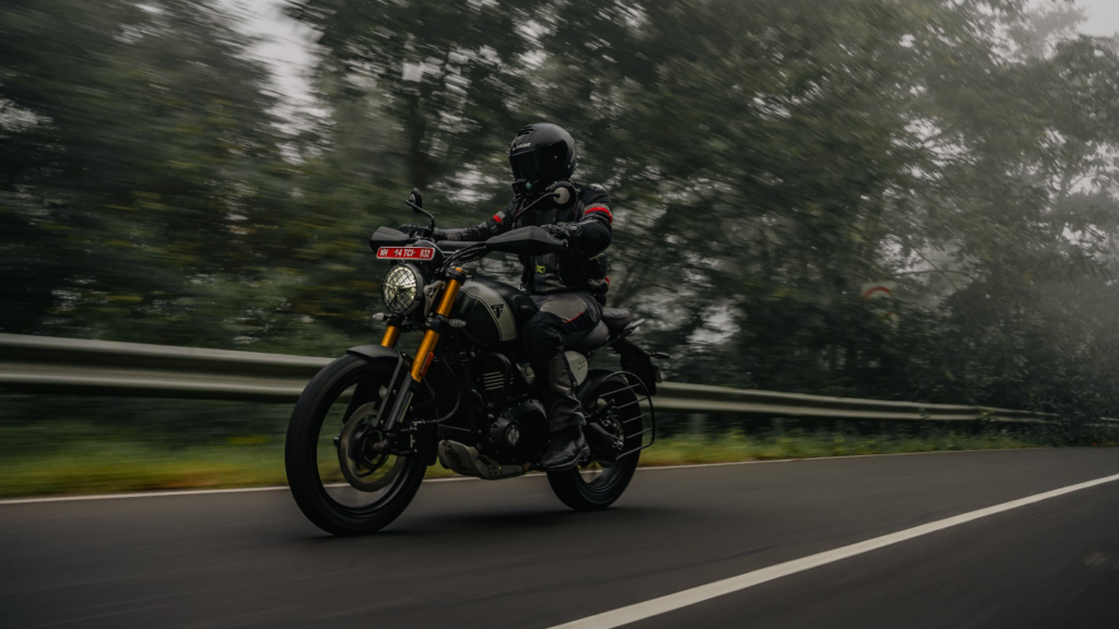 A motorcyclist in focus while riding a motorcycle on the road with trees captured in motion