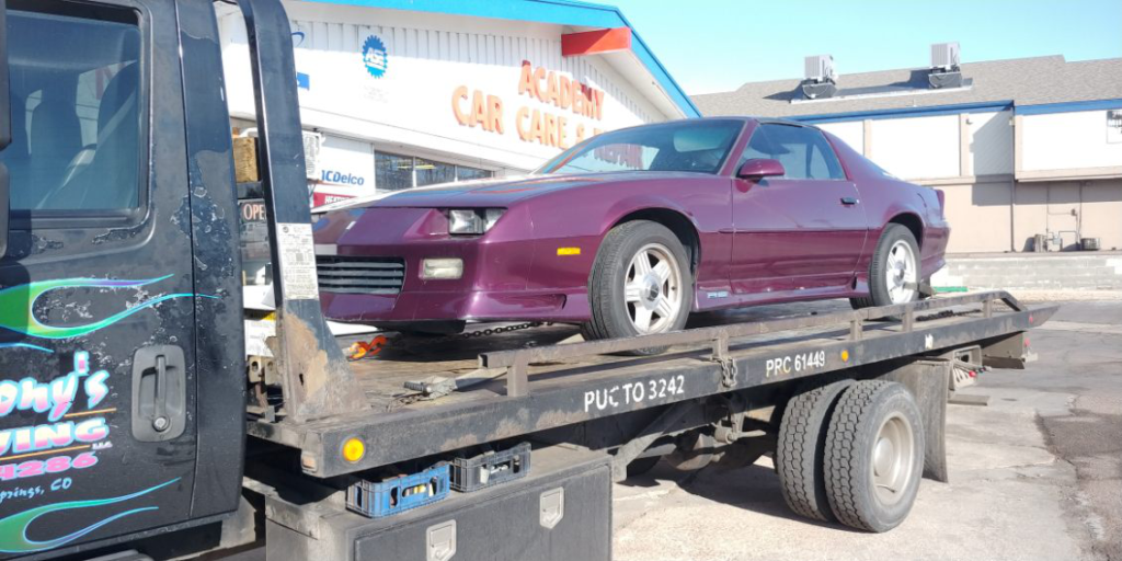  A burgundy car secured on an Anthony's Towing tow truck, positioned outside an automotive car garage, highlighting professional towing services.
