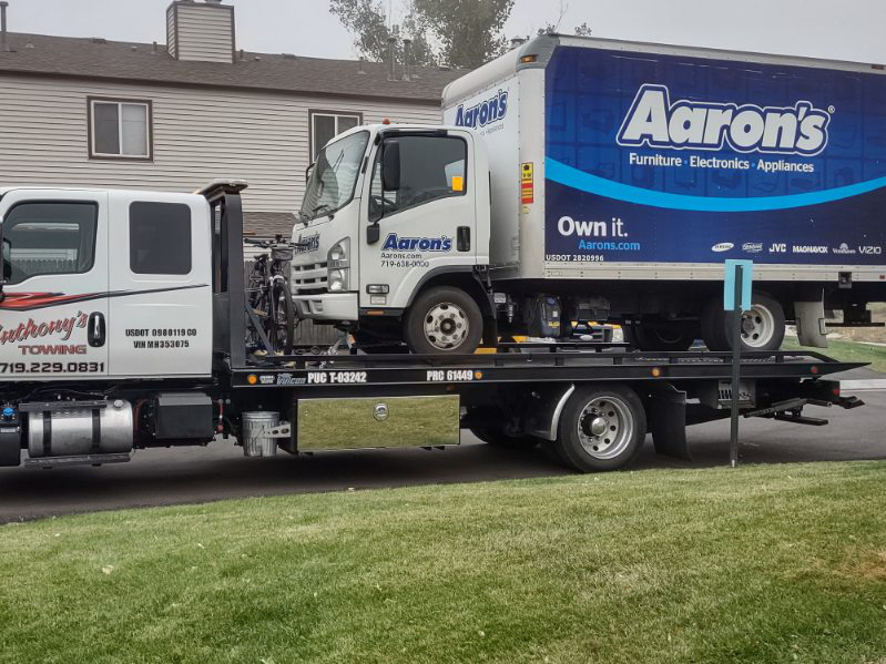 An Aaron's truck securely lifted atop an Anthony's Towing tow truck in a residential area, showcasing efficient and reliable towing services.